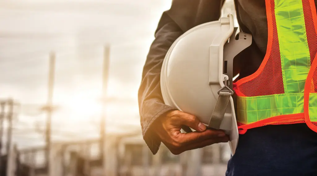 A construction worker wearing a reflective safety vest holds a white hard hat at their side, reflecting the strong safety culture and reliable labour hire standards of bout MIH, with an industrial site blurred in the background.