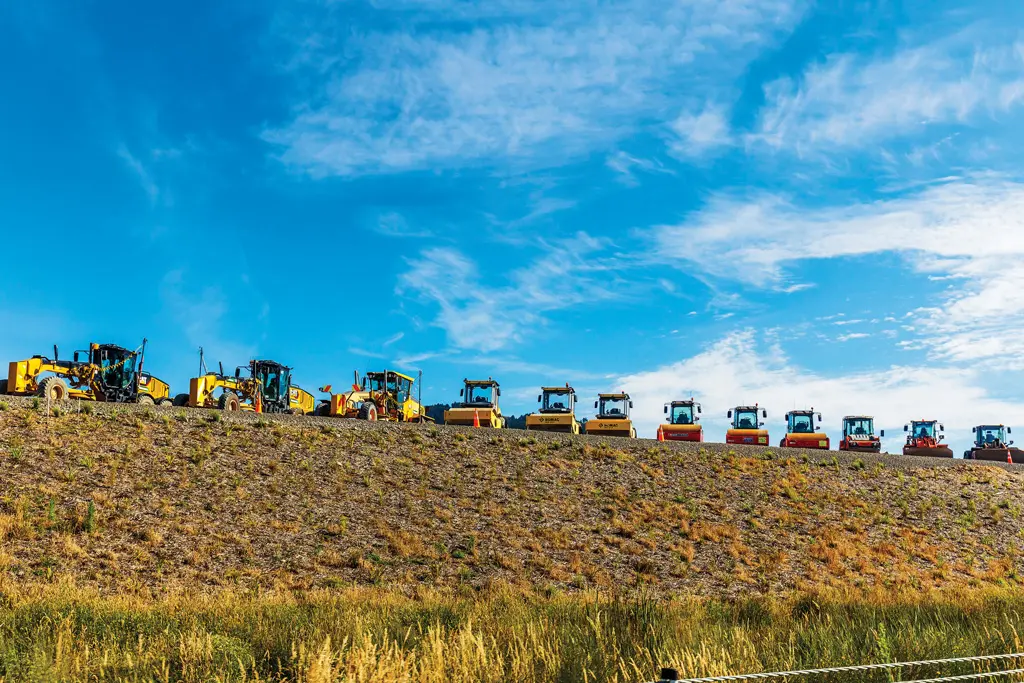 A row of construction vehicles, including graders and rollers, lined up on a sloped, grassy embankment under a bright blue sky highlights the expertise of Hunter Valley contractors in delivering top-tier mining services.